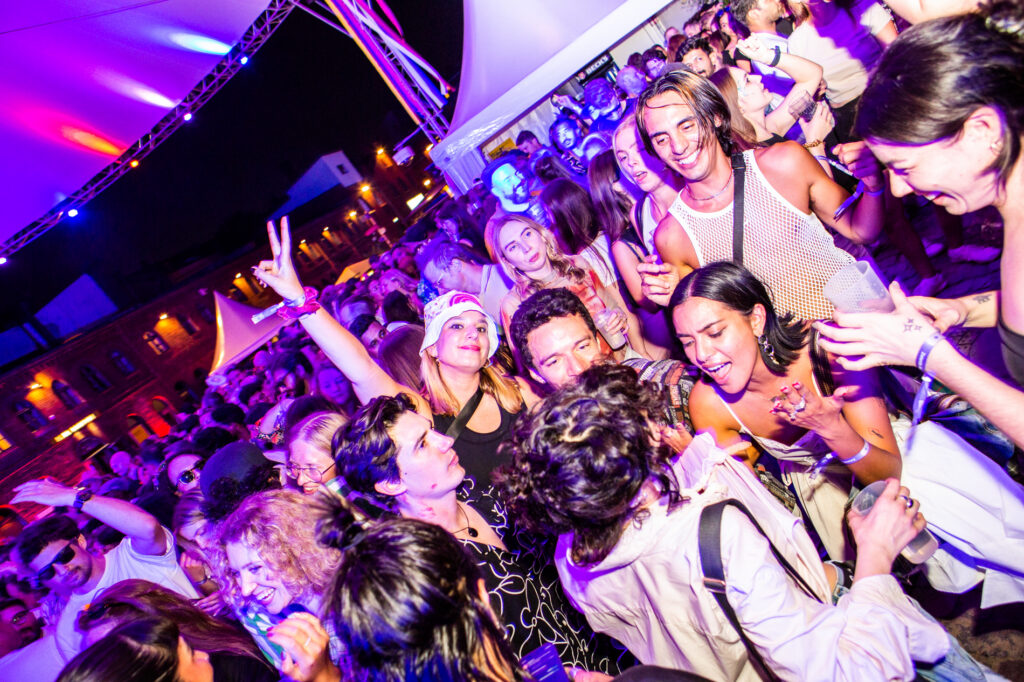 Feiernde Menge tanzt ausgelassen bei einem Outdoor-Event mit violetter Beleuchtung.