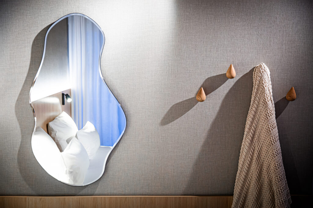 Hotelfotografie eines modernen Zimmers mit Wellenspiegel und minimalistischen Kleiderhaken.