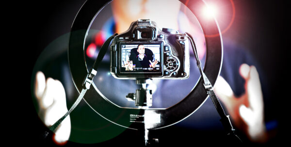 Blick durch ein Ringlicht auf eine DSLR-Kamera, die einen Mann bei einer Videoaufnahme zeigt.