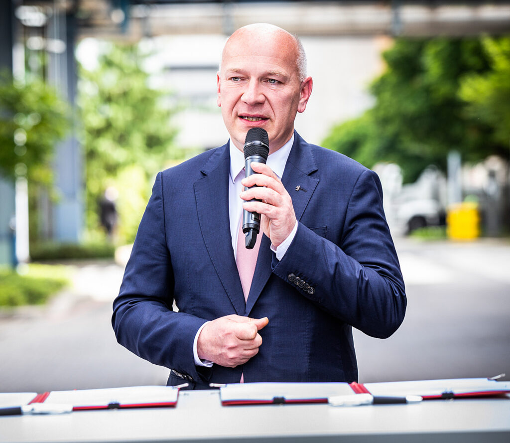 Nahaufnahme eines Redners mit Mikrofon bei einem Outdoor-Termin auf einem Firmengelände.